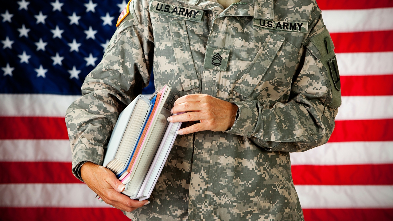 US military personnel in uniform holding books for school. The person is standing in front of an American flag backdrop. US military personnel in uniform holding books for school. The person is standing in front of an American flag backdrop.